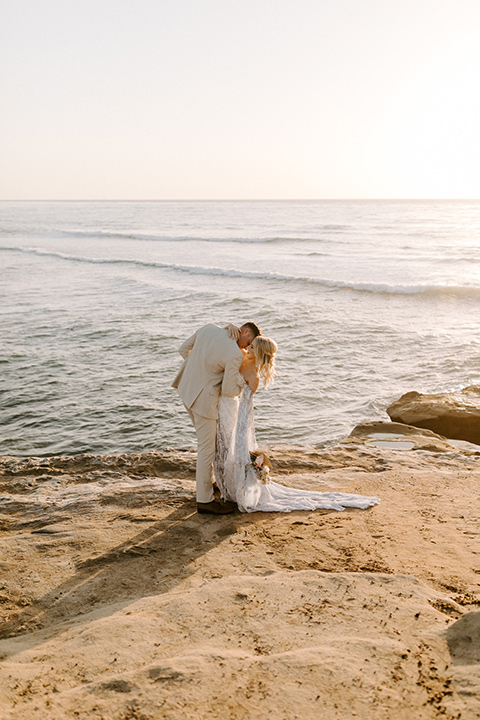  boho wedding with the ceremony inside and the reception on the cliffs overlooking the ocean and the bride in a finged gown and the groom in a tan suit 