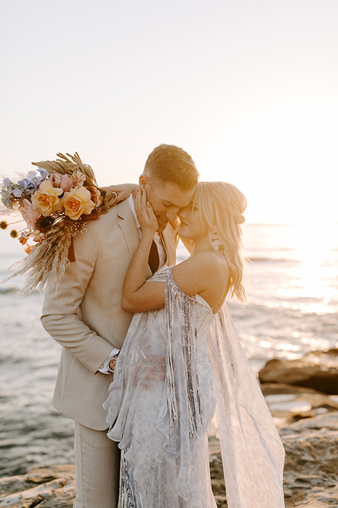  boho wedding with the ceremony inside and the reception on the cliffs overlooking the ocean and the bride in a finged gown and the groom in a tan suit 