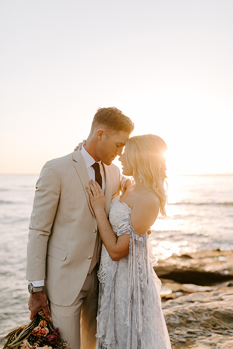  boho wedding with the ceremony inside and the reception on the cliffs overlooking the ocean and the bride in a finged gown and the groom in a tan suit 