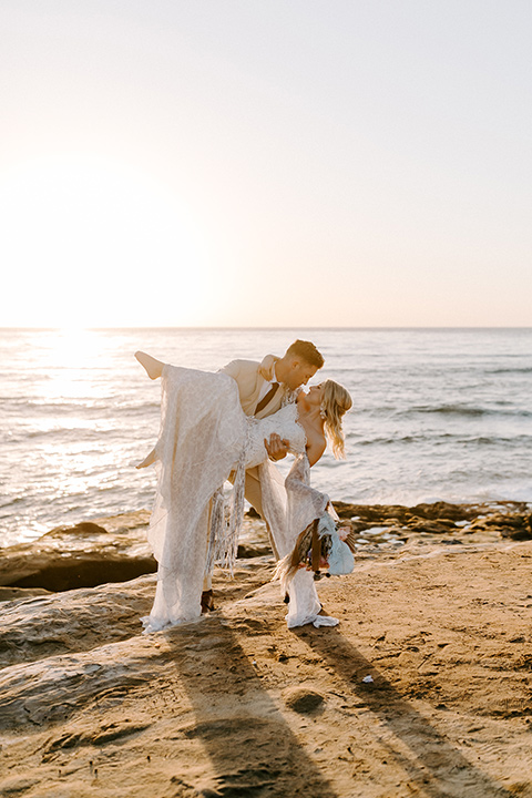  boho wedding with the ceremony inside and the reception on the cliffs overlooking the ocean and the bride in a finged gown and the groom in a tan suit 