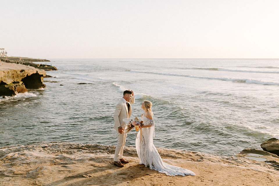  boho wedding with the ceremony inside and the reception on the cliffs overlooking the ocean and the bride in a finged gown and the groom in a tan suit 