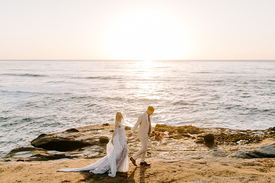  boho wedding with the ceremony inside and the reception on the cliffs overlooking the ocean and the bride in a finged gown and the groom in a tan suit 