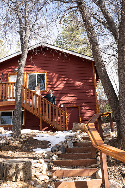  big bear elopement in the snow with the bride is a lace gown and the groom in a green suit – couple leaving the cabin