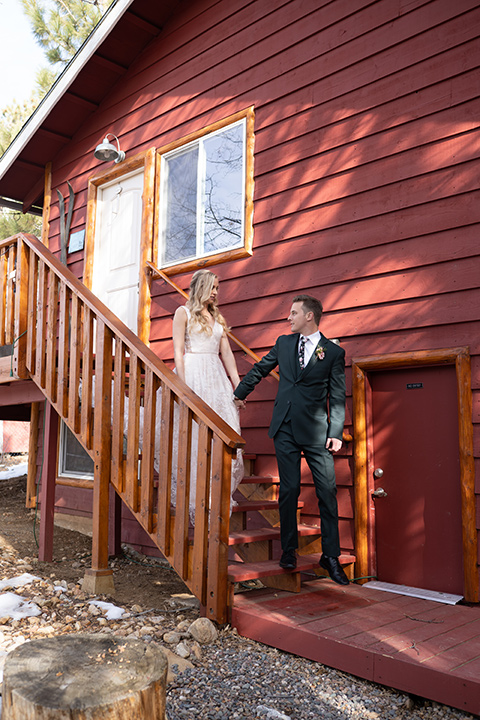  big bear elopement in the snow with the bride is a lace gown and the groom in a green suit – couple leaving the cabin 