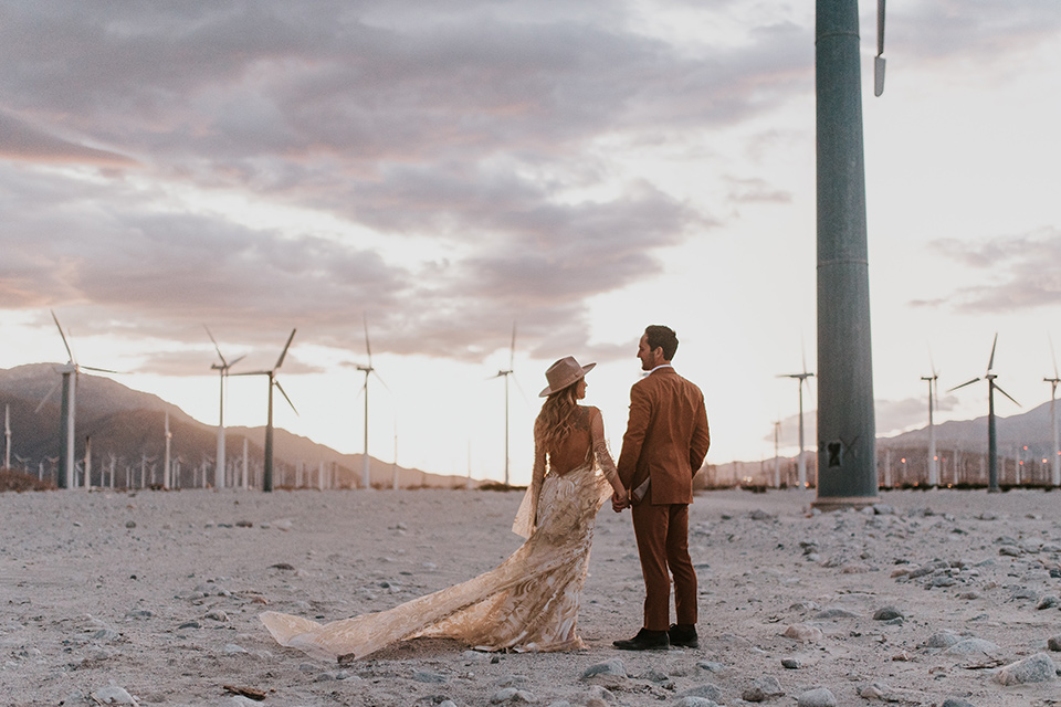  eloping in the desert with a bohemian vibe – bride in a lace gown and the groom in a caramel brown suit – couple at sunset 