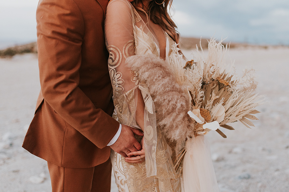  eloping in the desert with a bohemian vibe – bride in a lace gown and the groom in a caramel brown suit – couple embracing close up shot 