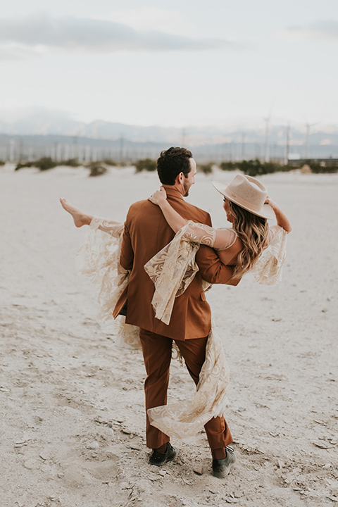  eloping in the desert with a bohemian vibe – bride in a lace gown and the groom in a caramel brown suit -couple dancing and spinning