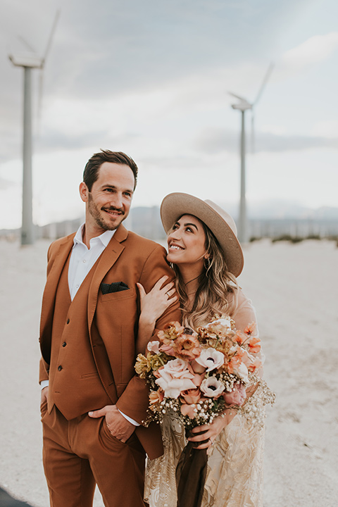  eloping in the desert with a bohemian vibe – bride in a lace gown and the groom in a caramel brown suit - couple embracing 