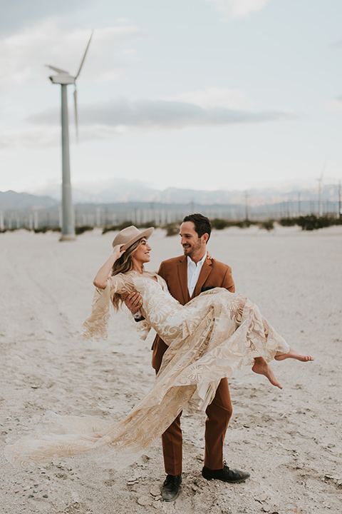  eloping in the desert with a bohemian vibe – bride in a lace gown and the groom in a caramel brown suit - couple dancing and spinning 