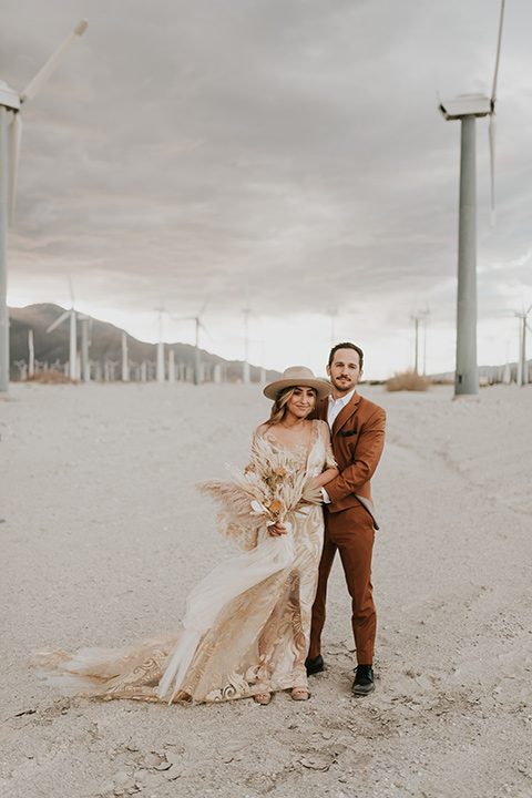  eloping in the desert with a bohemian vibe – bride in a lace gown and the groom in a caramel brown suit - couple embracing 