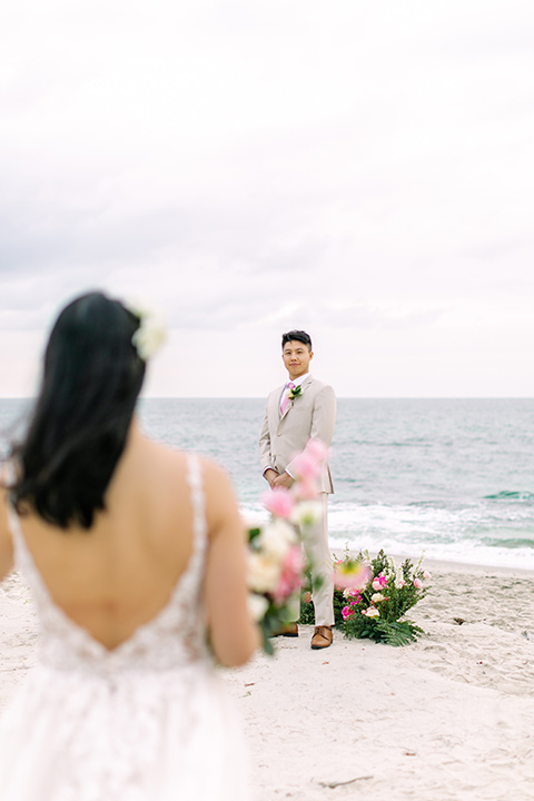  a coastal beach theme with a blush and beige wedding color scheme – bride in her gown walking down the aisle to her groom 