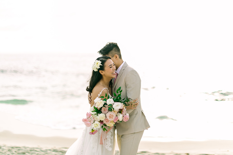  a coastal beach theme with a blush and beige wedding color scheme – couple hugging on the sand