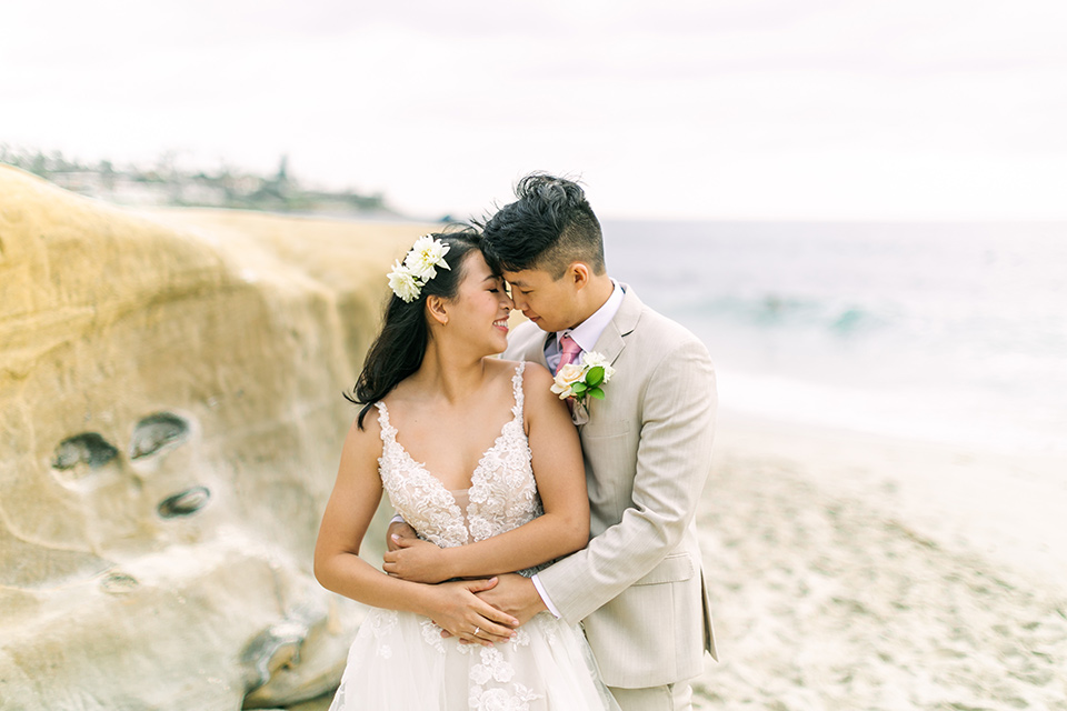  a coastal beach theme with a blush and beige wedding color scheme – couple embracing on the sand