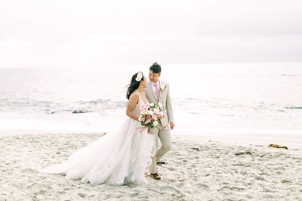  a coastal beach theme with a blush and beige wedding color scheme – couple walking on the sand