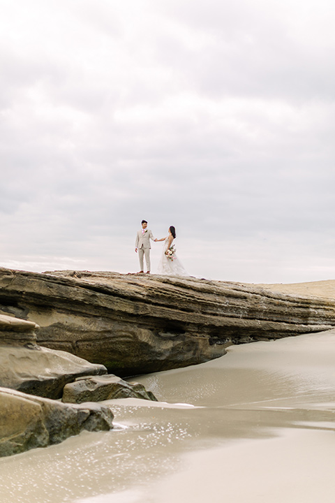  a coastal beach theme with a blush and beige wedding color scheme – couple walking on the cliffs 