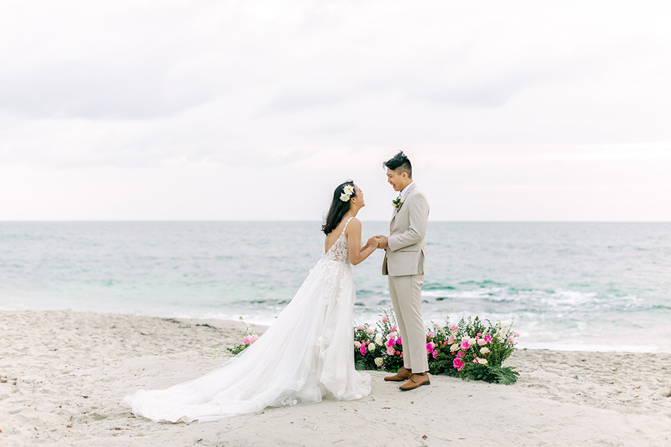  a coastal beach theme with a blush and beige wedding color scheme – couple exchanging vows on the sand