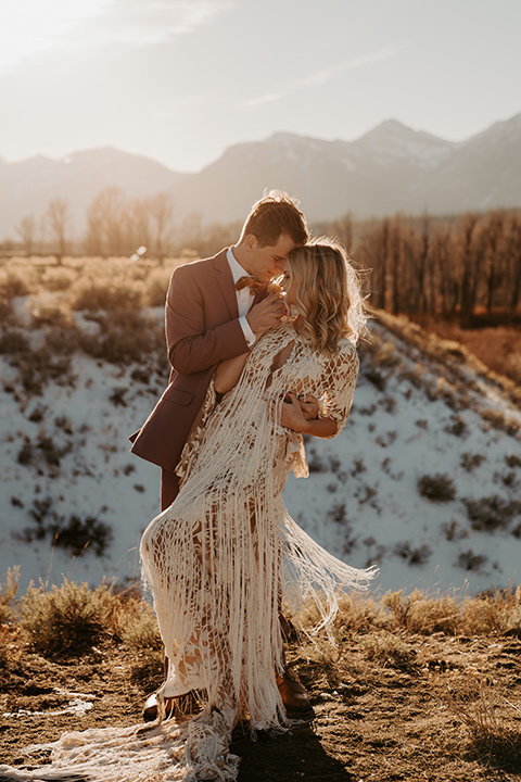  grand tetons elopement in the winter with snow on the ground with the bride in a lace gown and the groom in a rose pink suit – couple dancing in the meadow