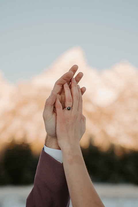  grand tetons elopement in the winter with snow on the ground with the bride in a lace gown and the groom in a rose pink suit – hands in the air with the rings