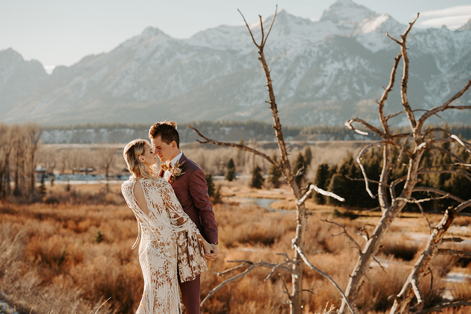  grand tetons elopement in the winter with snow on the ground with the bride in a lace gown and the groom in a rose pink suit – couple kissing in the meadow 