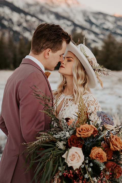  grand tetons elopement in the winter with snow on the ground with the bride in a lace gown and the groom in a rose pink suit – couple kissing 