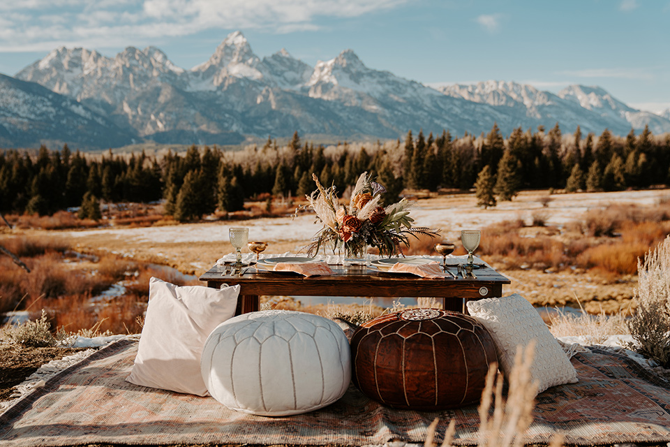  grand tetons elopement in the winter with snow on the ground with the bride in a lace gown and the groom in a rose pink suit – couple sitting at a picnic 