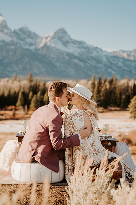  grand tetons elopement in the winter with snow on the ground with the bride in a lace gown and the groom in a rose pink suit – couple sitting