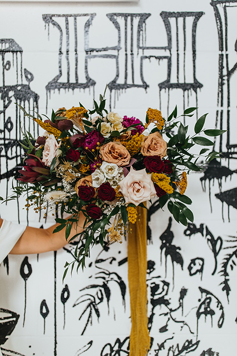  modern and colorful wedding with the bride in an off-the-shoulder dress and the groom in an all-black tuxedo – floral bouquet 