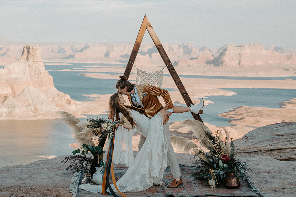  a boho wedding at lake powell with the bride in a bohemian gown and a wide brimmed hat and the groom in a gold velvet jacket – couple kissing at the ceremony space