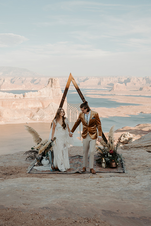  a boho wedding at lake powell with the bride in a bohemian gown and a wide brimmed hat and the groom in a gold velvet jacket – couple at wedding ceremony