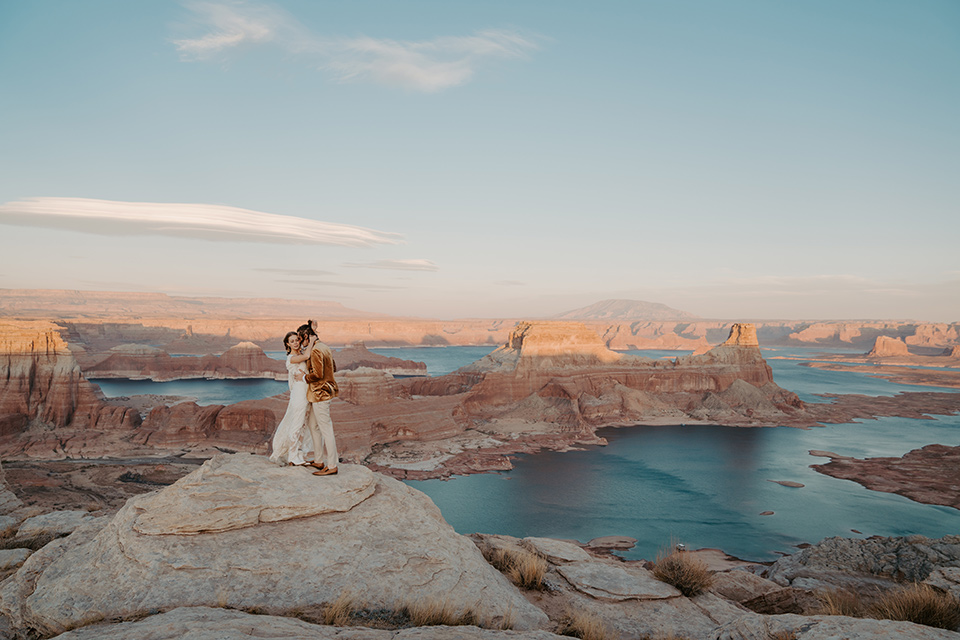  a boho wedding at lake powell with the bride in a bohemian gown and a wide brimmed hat and the groom in a gold velvet jacket – couple on the cliff