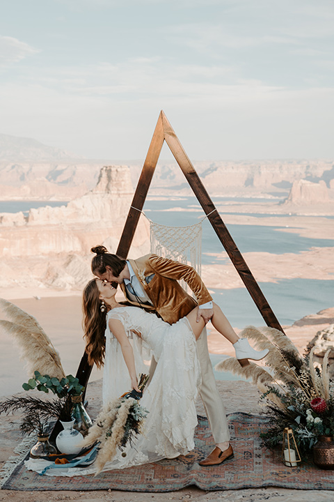  a boho wedding at lake powell with the bride in a bohemian gown and a wide brimmed hat and the groom in a gold velvet jacket – couple at wedding ceremony 