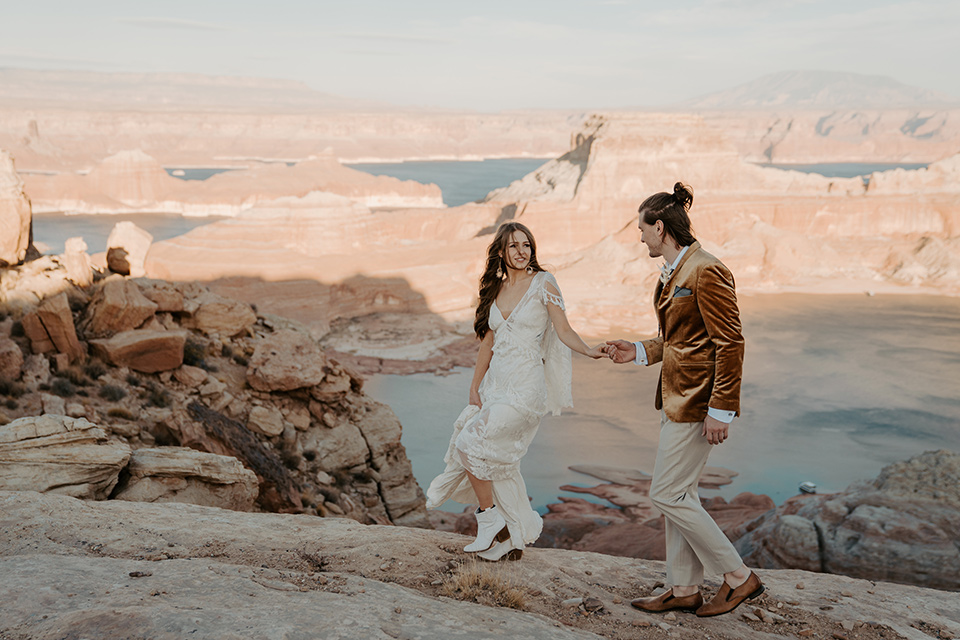  a boho wedding at lake powell with the bride in a bohemian gown and a wide brimmed hat and the groom in a gold velvet jacket – couple walking